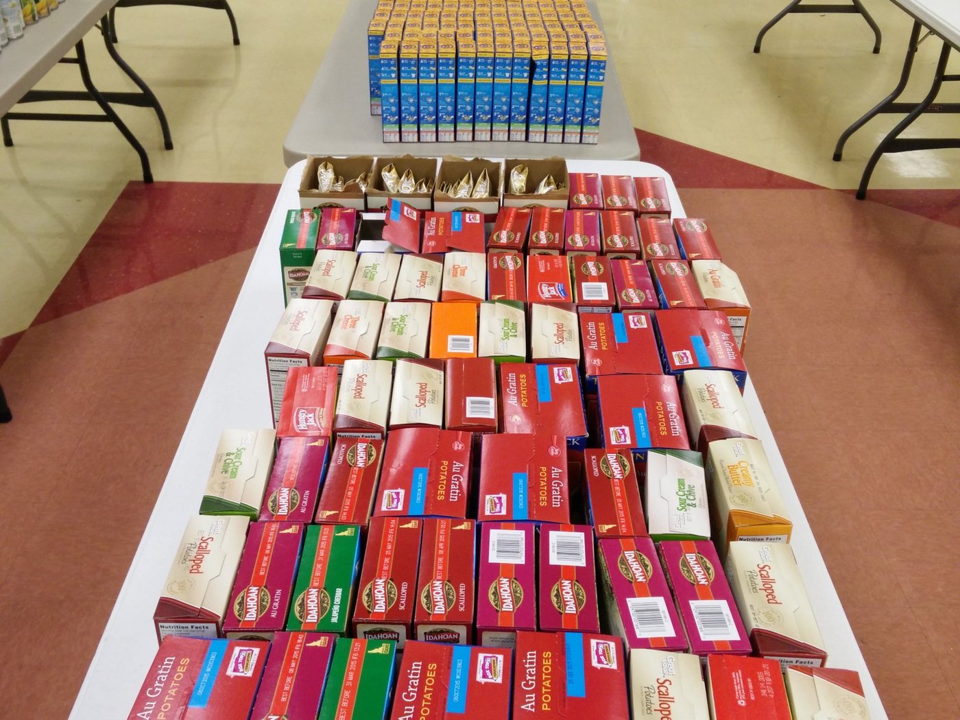 Tables stacked with donated boxed potatoes, macaroni and canned vegetables from a food drive