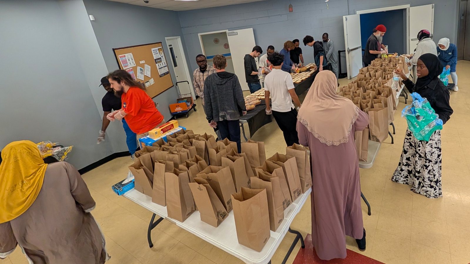 Volunteers packing brown-bag lunches and making sandwiches across long tables in the Clifton Mosque basement